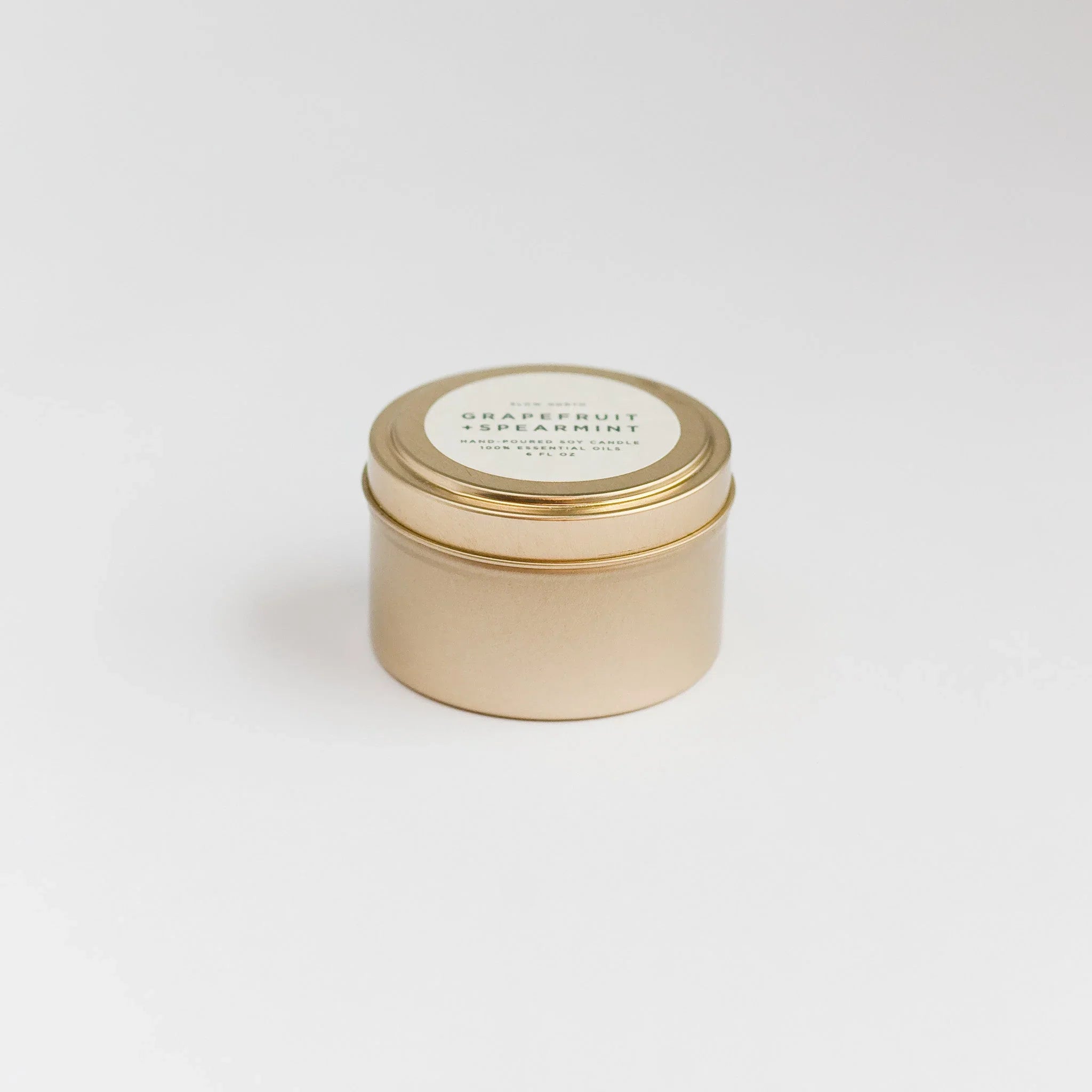 Gold travel tin candle labeled Grapefruit + Spearmint hand-poured soy candle on white background