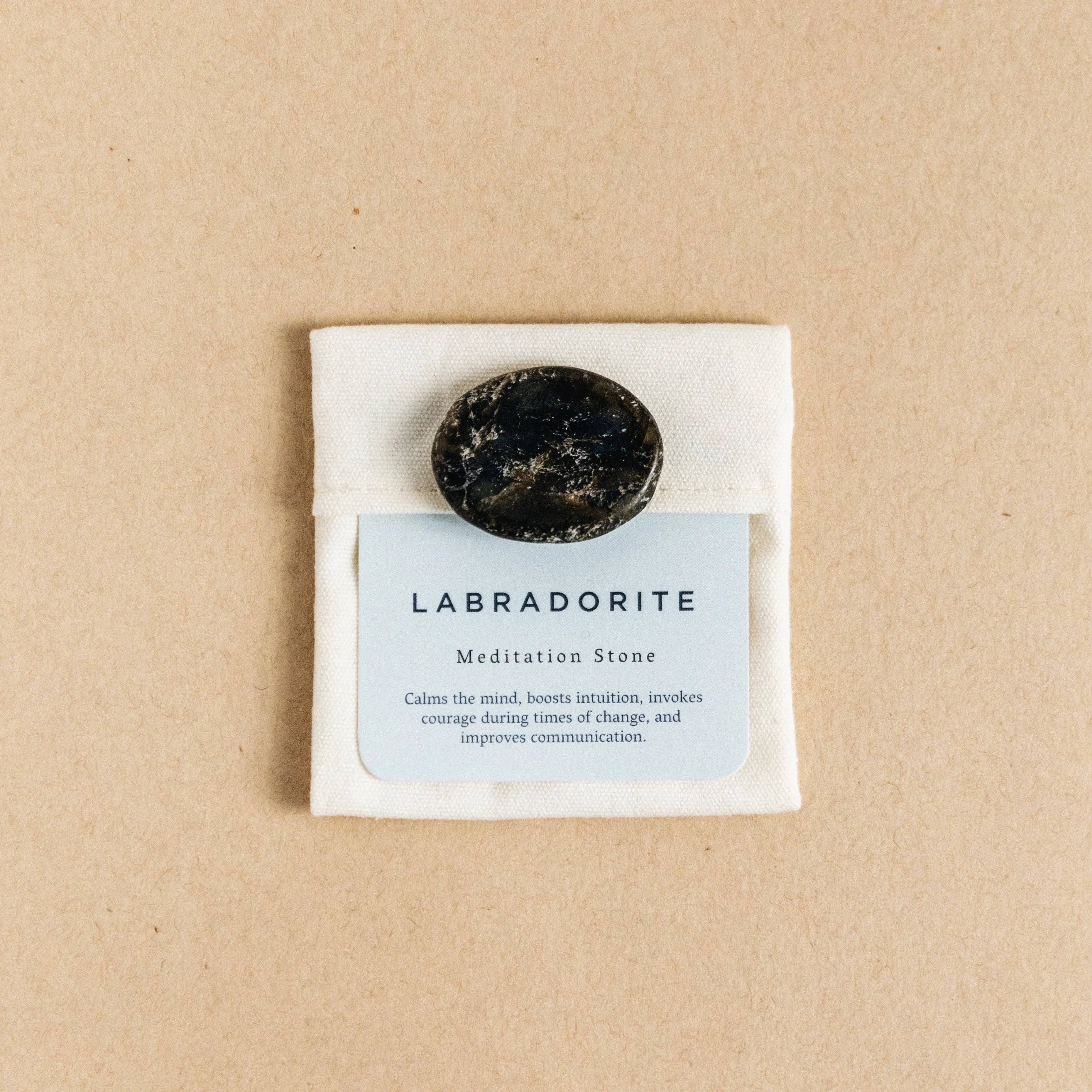 Polished black labradorite meditation stone on white pouch with descriptive card on beige background
